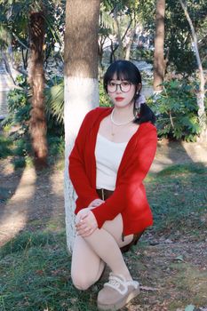 Elegant woman wearing red sweater in a Nanjing park, capturing serene beauty and nature.