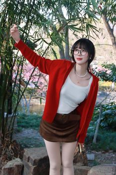 Stylish young woman in red jacket posing in a park, enjoying a sunny day.