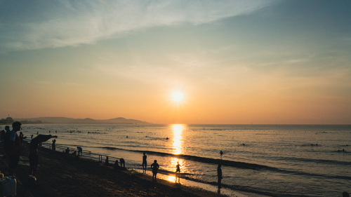 Free A serene beach scene at sunset with silhouetted figures enjoying the evening waves. Stock Photo
