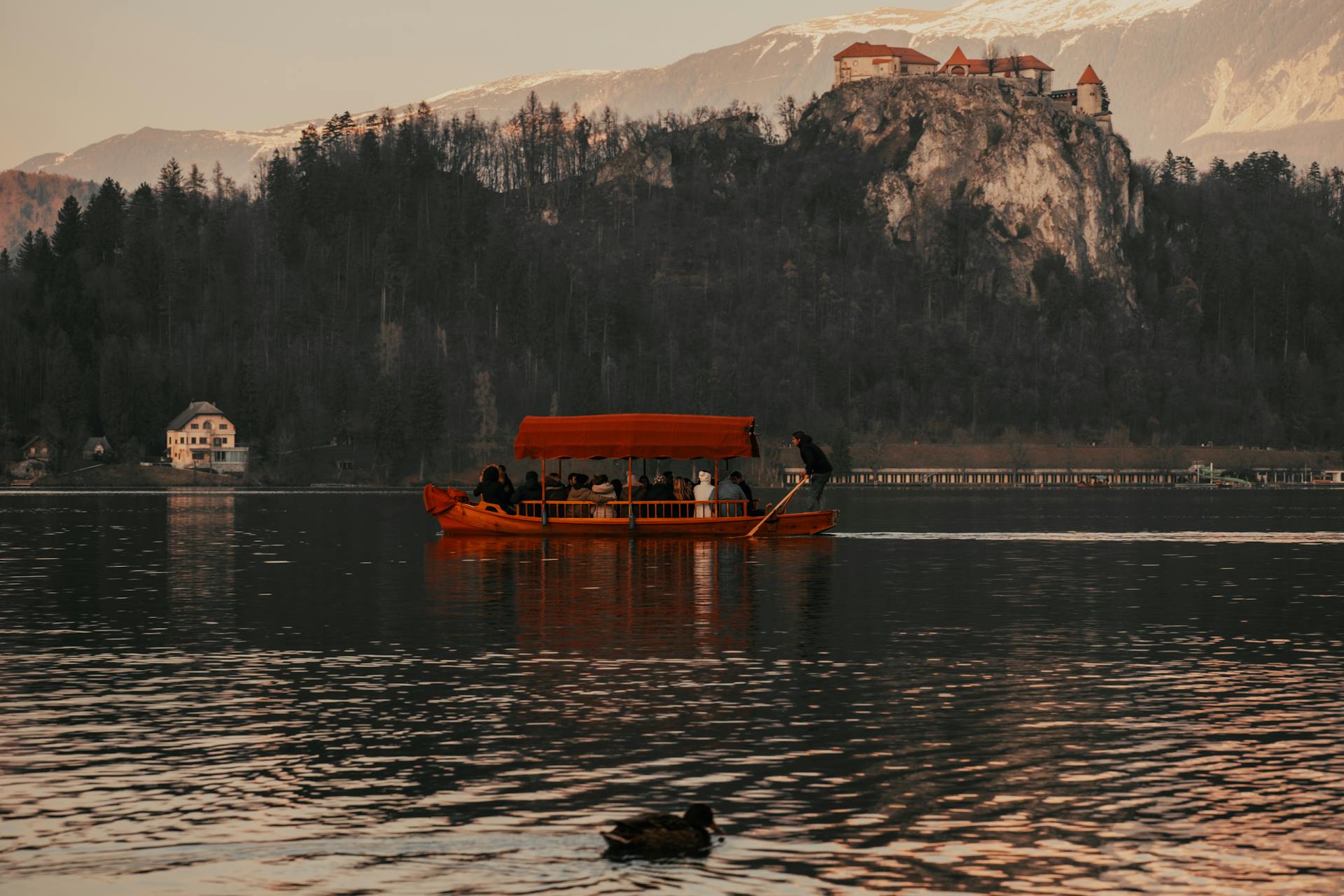 A traditional Pletna boat glides across Lake Bled with a view of Bled Castle amidst a serene landscape.