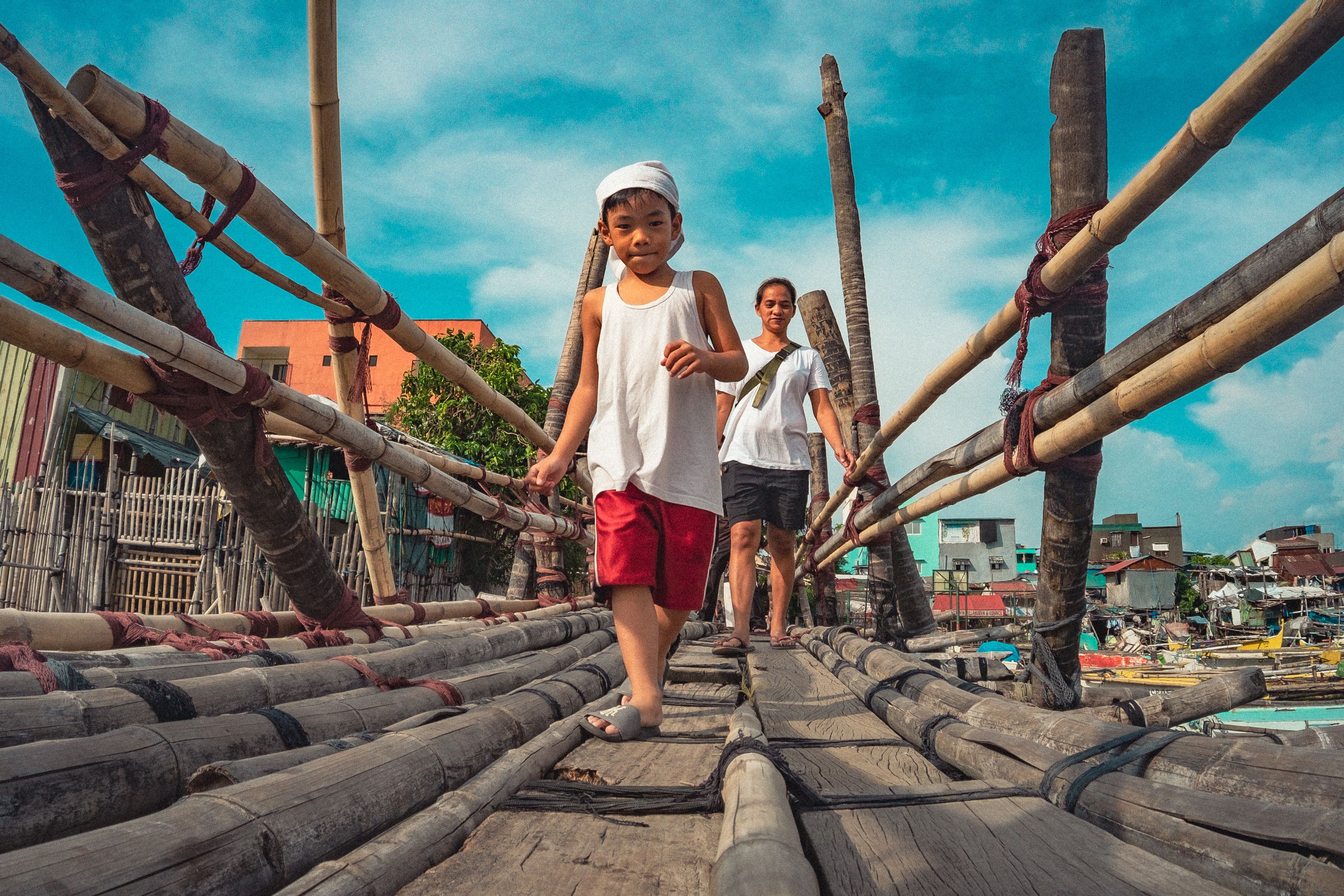 Two children crossing a rustic bamboo bridge in Navotas, Manila, Philippines on a sunny day.