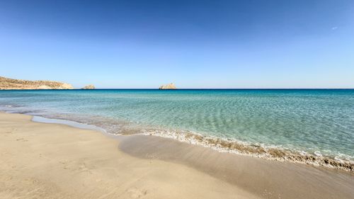 Free Peaceful sandy beach with crystal-clear water under a bright blue sky, perfect for relaxation. Stock Photo