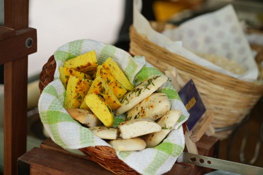 A wicker basket with assorted freshly baked bread topped with herbs and spices, placed on a checkered cloth.
