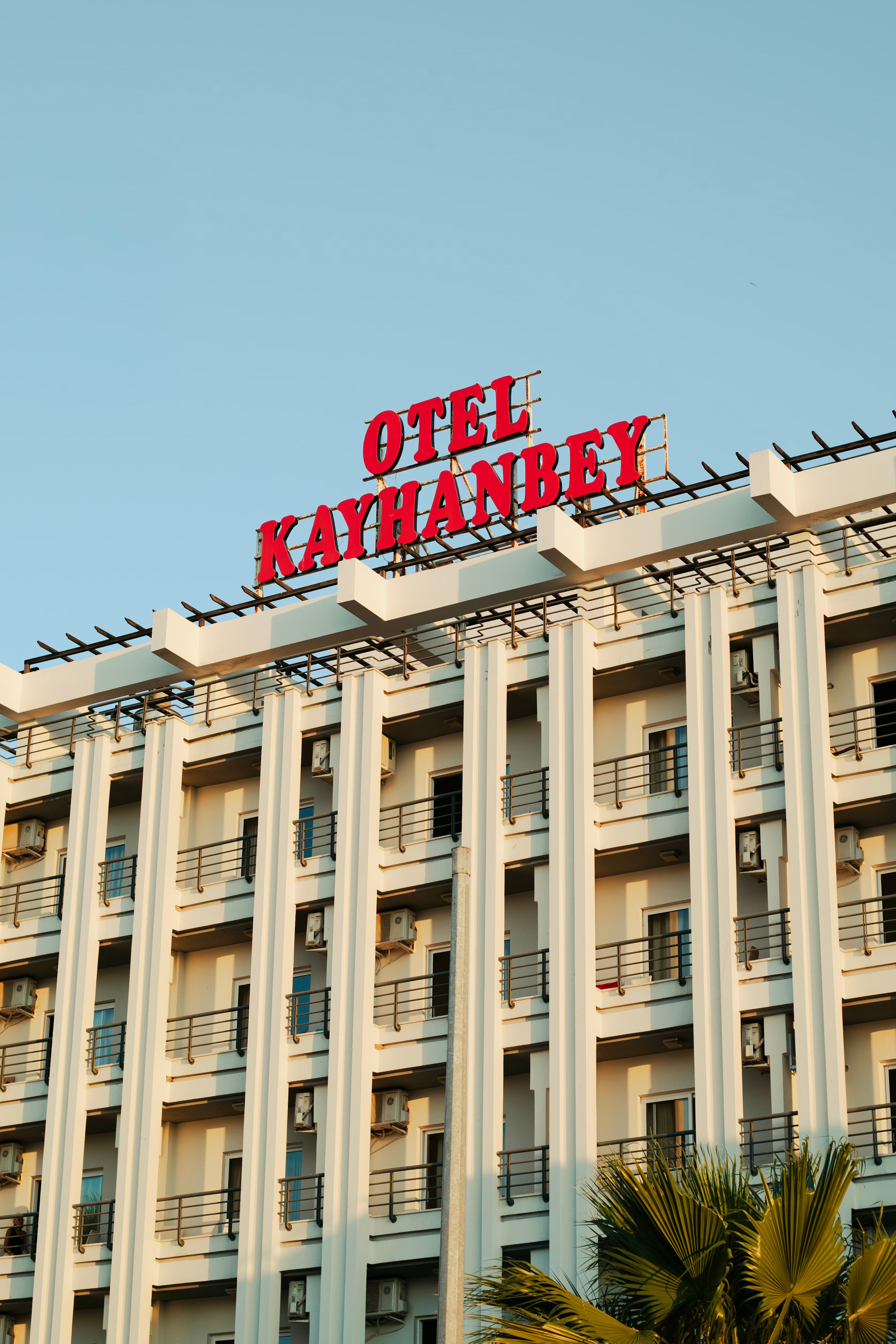 Exterior view of a modern hotel building with striking red signage against a clear sky.