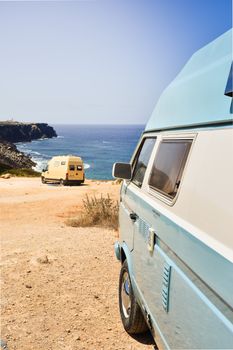 Two colorful camper vans enjoy scenic ocean views on a sunny day in Algarve, Portugal.