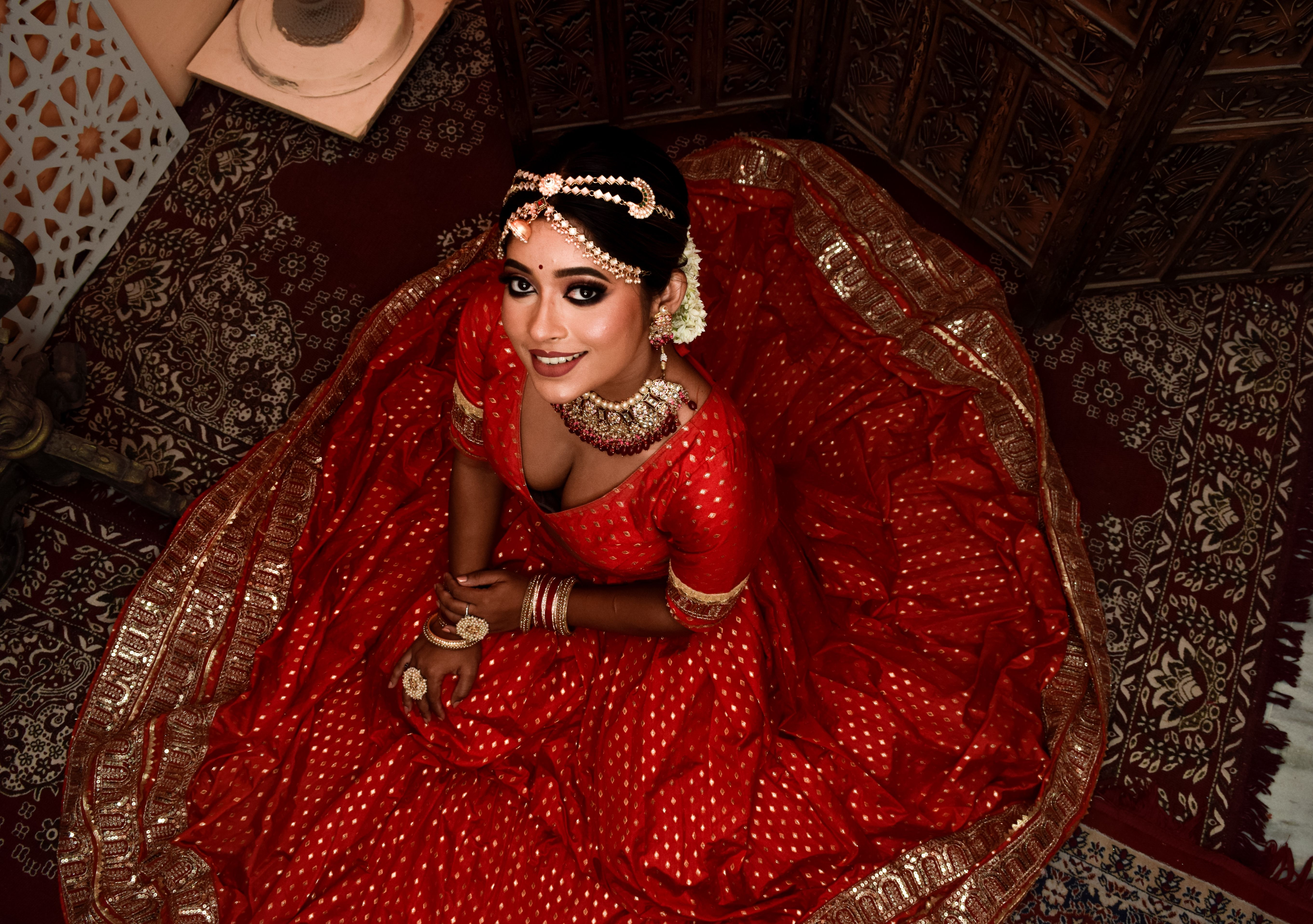 Captivating Indian bride in a red lehenga with intricate jewelry, seen from above.