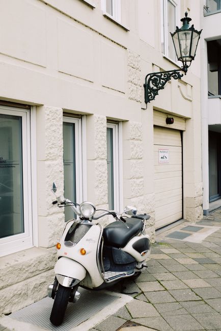 Vintage white scooter parked on sidewalk near window of modern building on sunny street in city