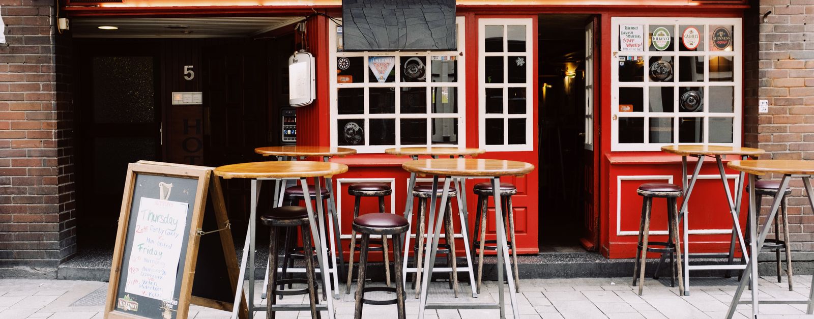 Empty terrace of local pub with empty tables and chairs against facade red window on sunny day in city