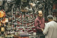 Seller interacting with customer in traditional white Arab clothes in typical oriental souvenir shop with numerous cozy lamps and swords