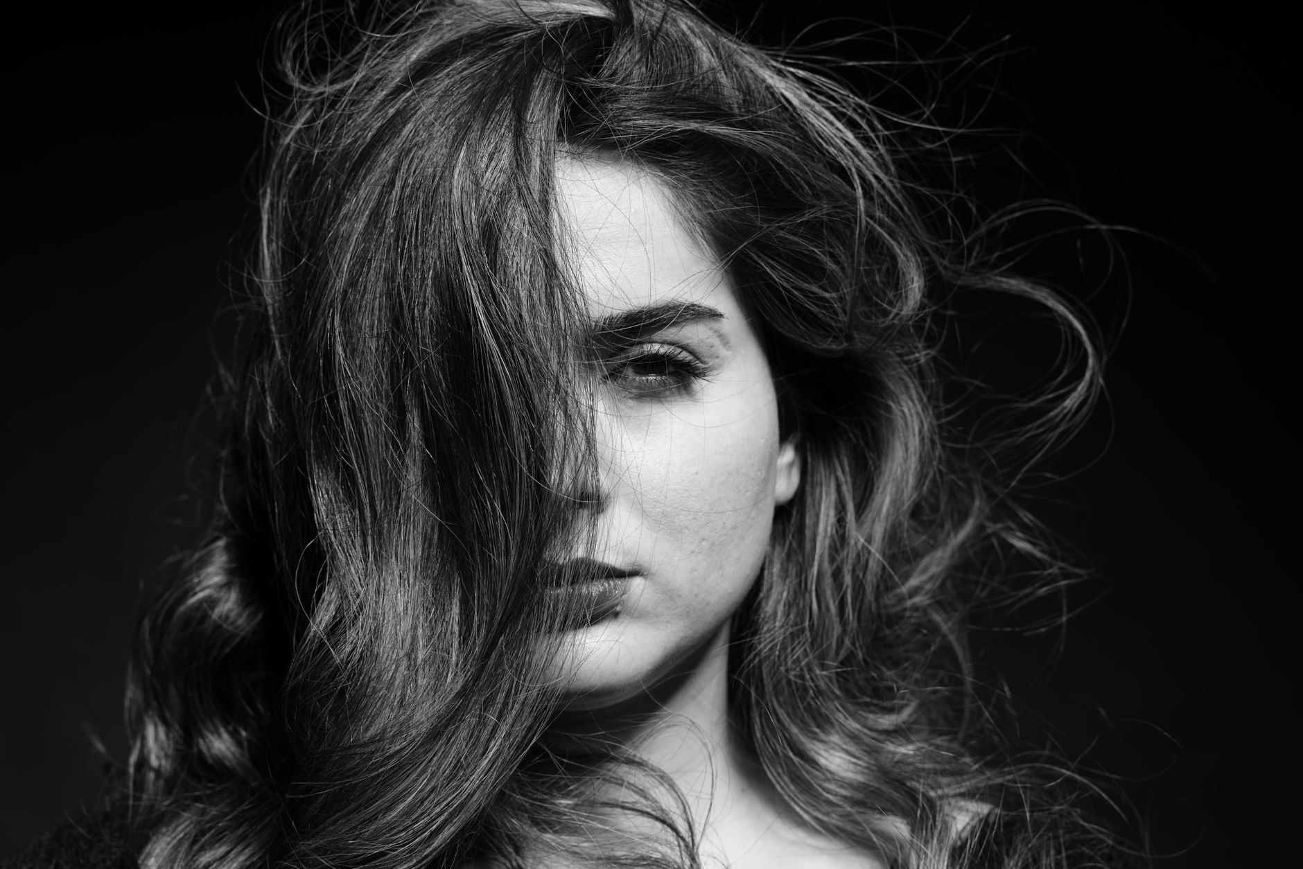 Artistic black and white portrait capturing an intense gaze with dynamic hair motion.
