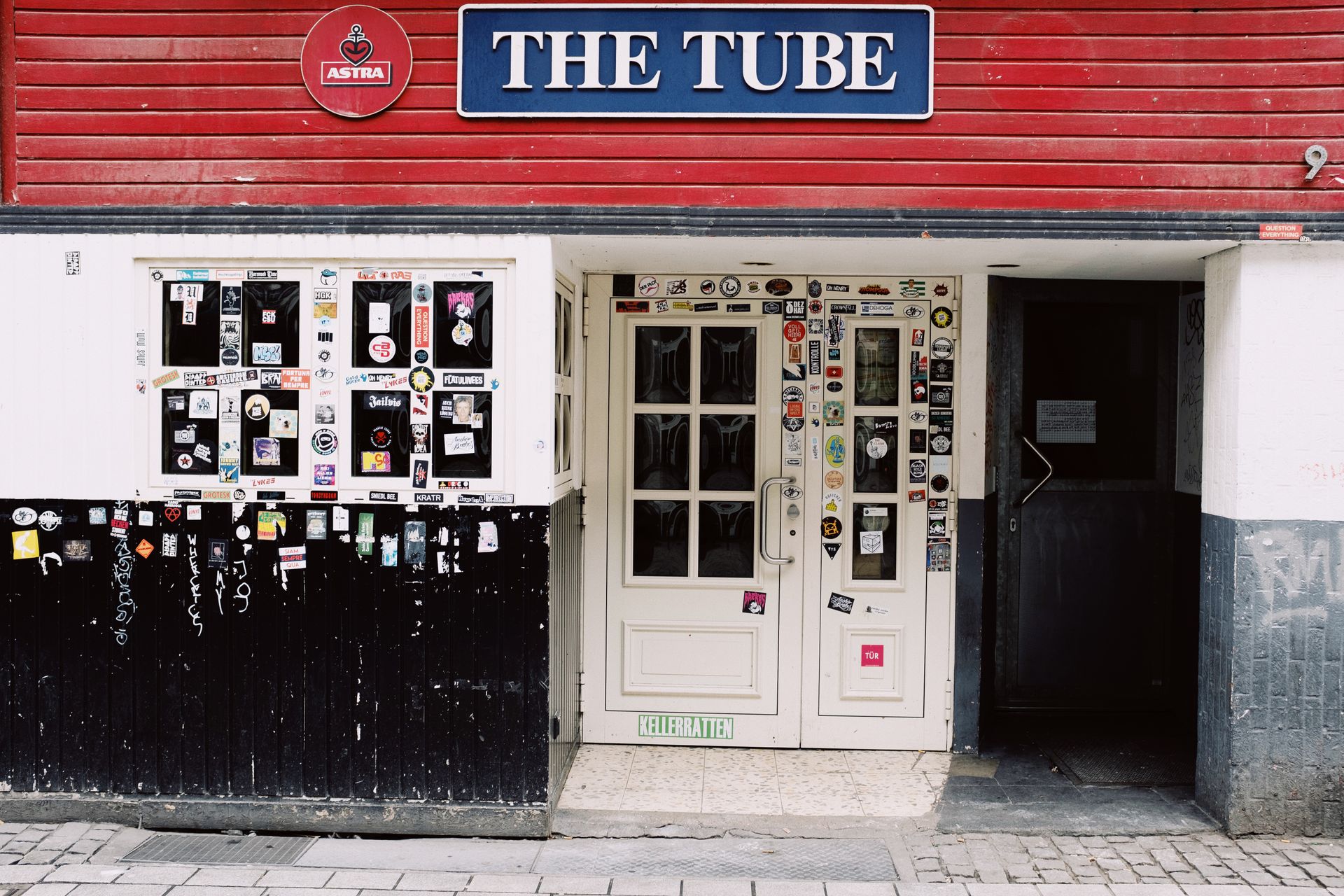 Exterior of closed pub with blue sign above entrance decorated with graffiti and colorful stickers