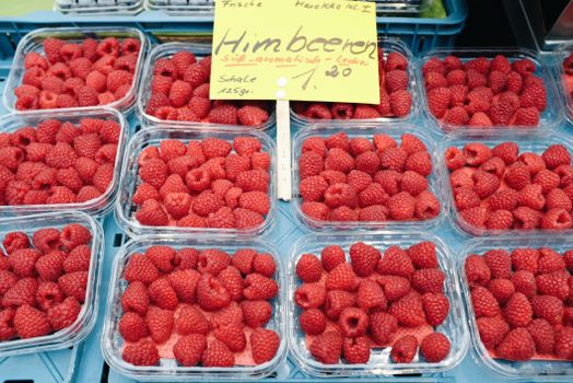 From above of arranged plastic containers filled with with fresh ripe raspberries placed on stall in street market