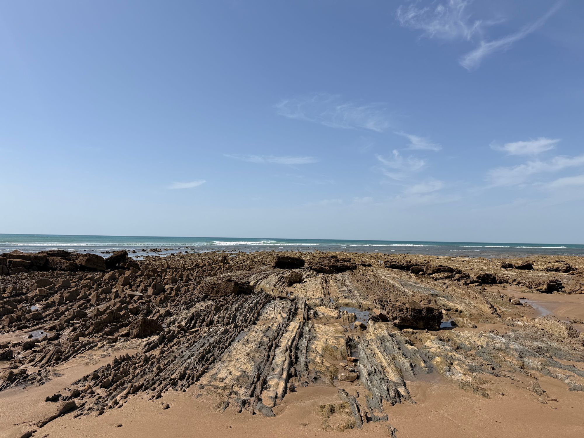 Vast rocky shoreline of Cabo Negro Beach under a clear blue sky, Morocco.