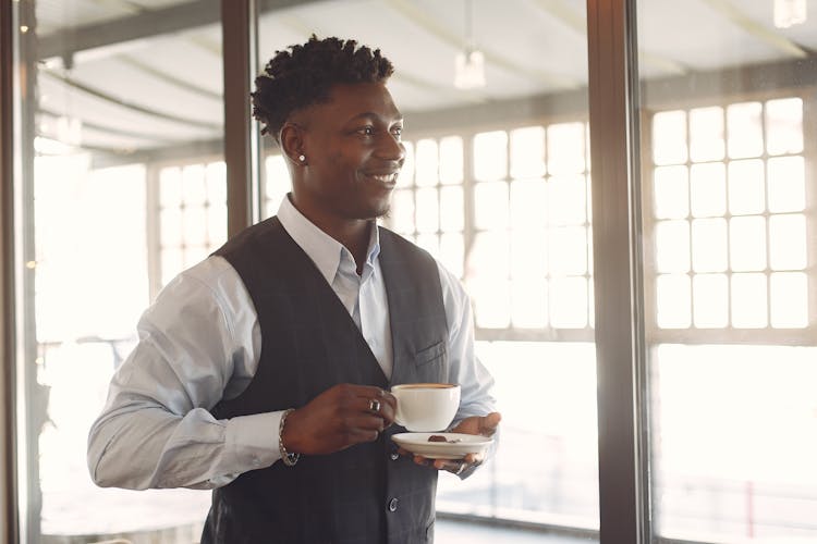 Smiling Young Ethnic Man Drinking Coffee In Cafe Near Window