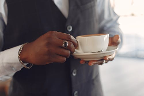 Free Crop unrecognizable African American man in formal suit holding cup of fresh coffee in hands while standing in modern light cafe Stock Photo