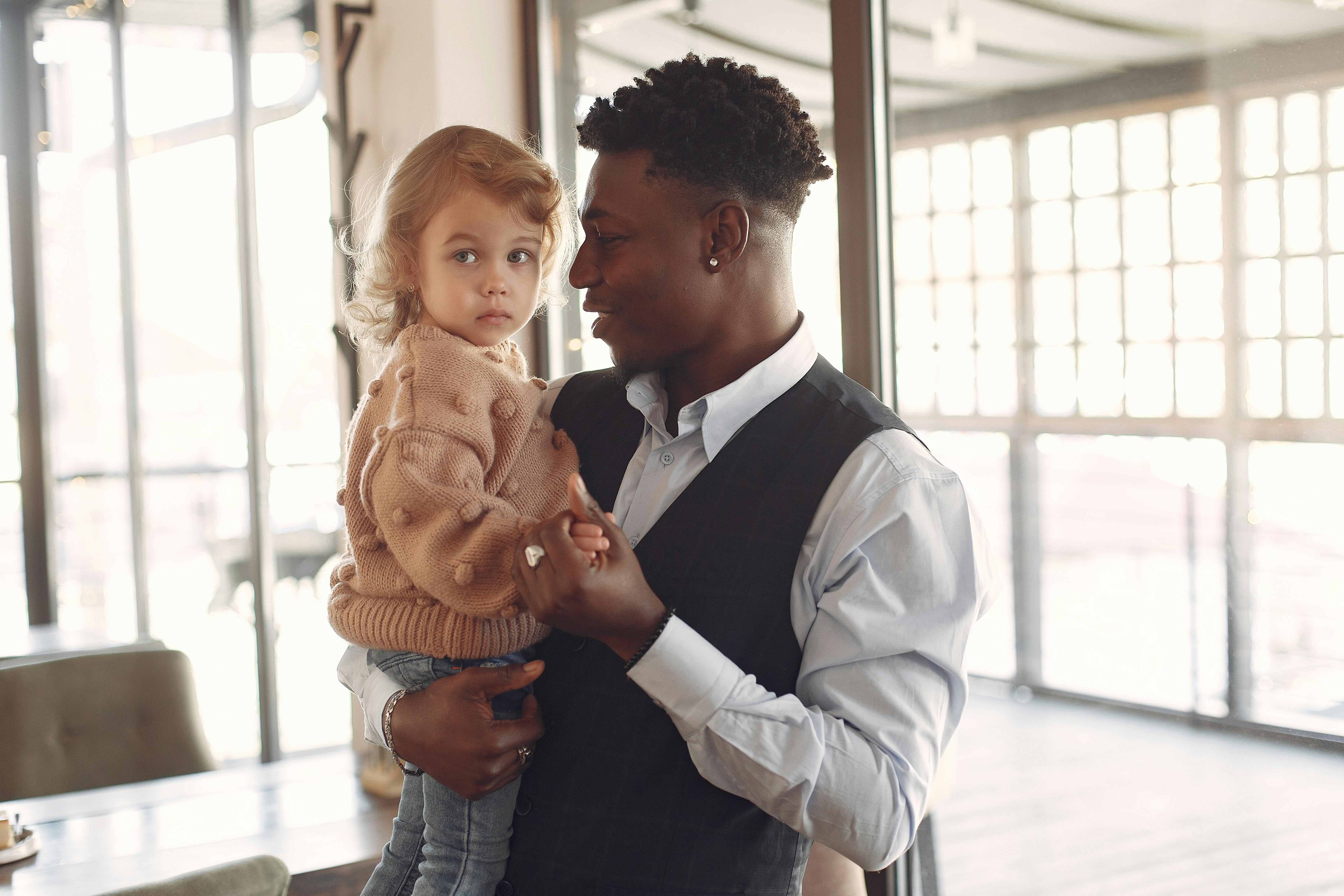 positive ethnic man holding little girl on hands while standing in cafe