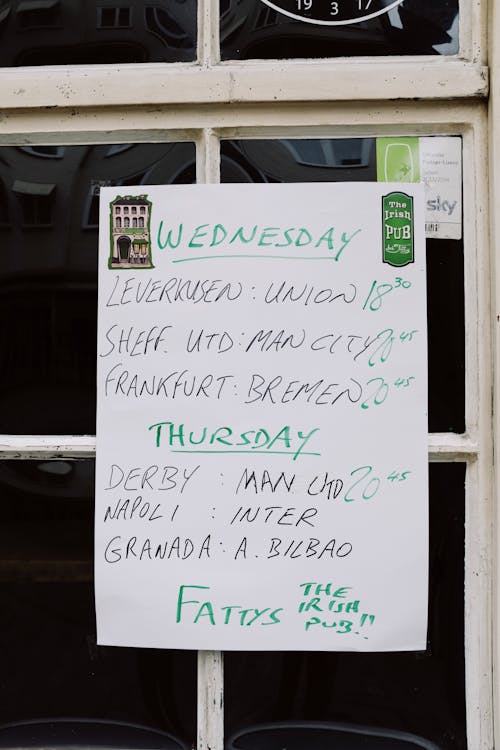 White blackboard with handwritten timetable hanging on glass door on entrance of pub