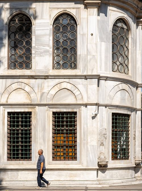 Free A person walks past an ornate marble facade with arched windows on a sunny day. Stock Photo