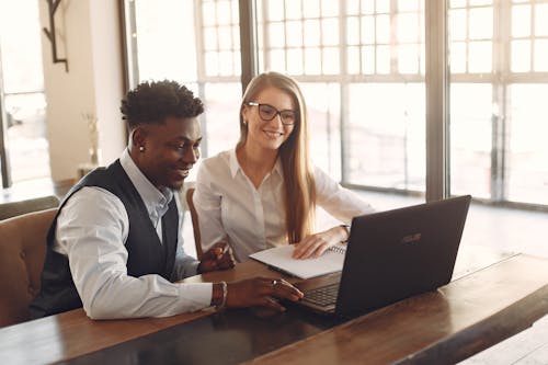 Positive multiethnic coworkers discussing business ideas while working on laptop in workspace