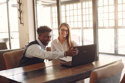 Cheerful multiracial business partners gathering together in modern workspace with laptop