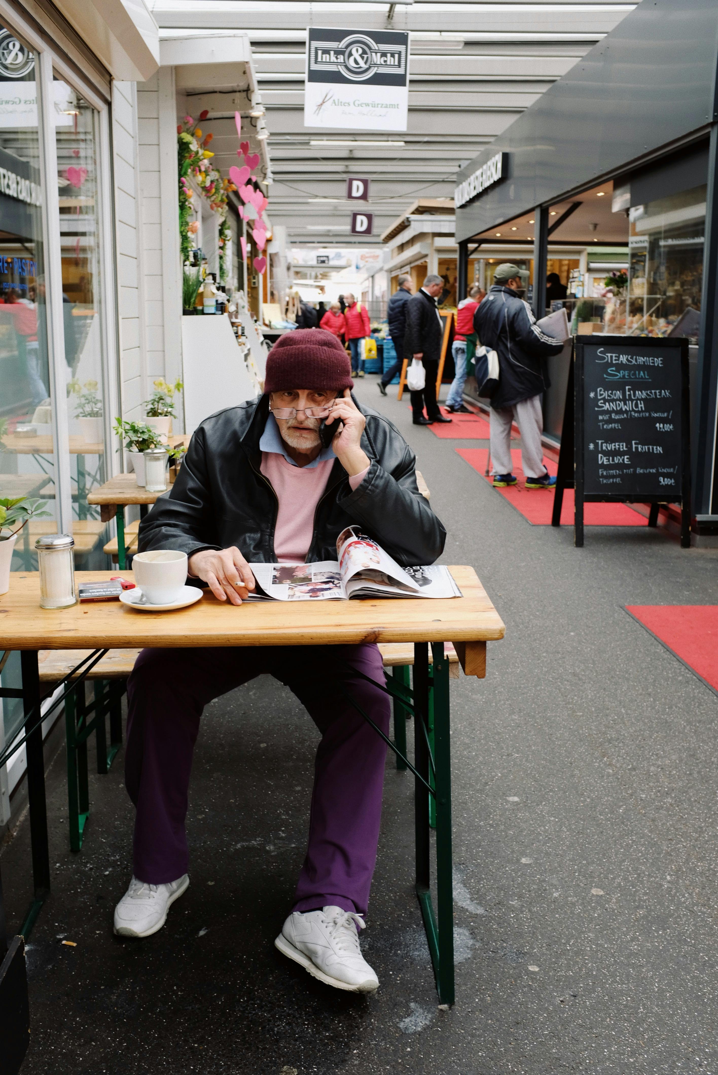 aged man reading newspaper and talking on smartphone while having coffee break in street cafe