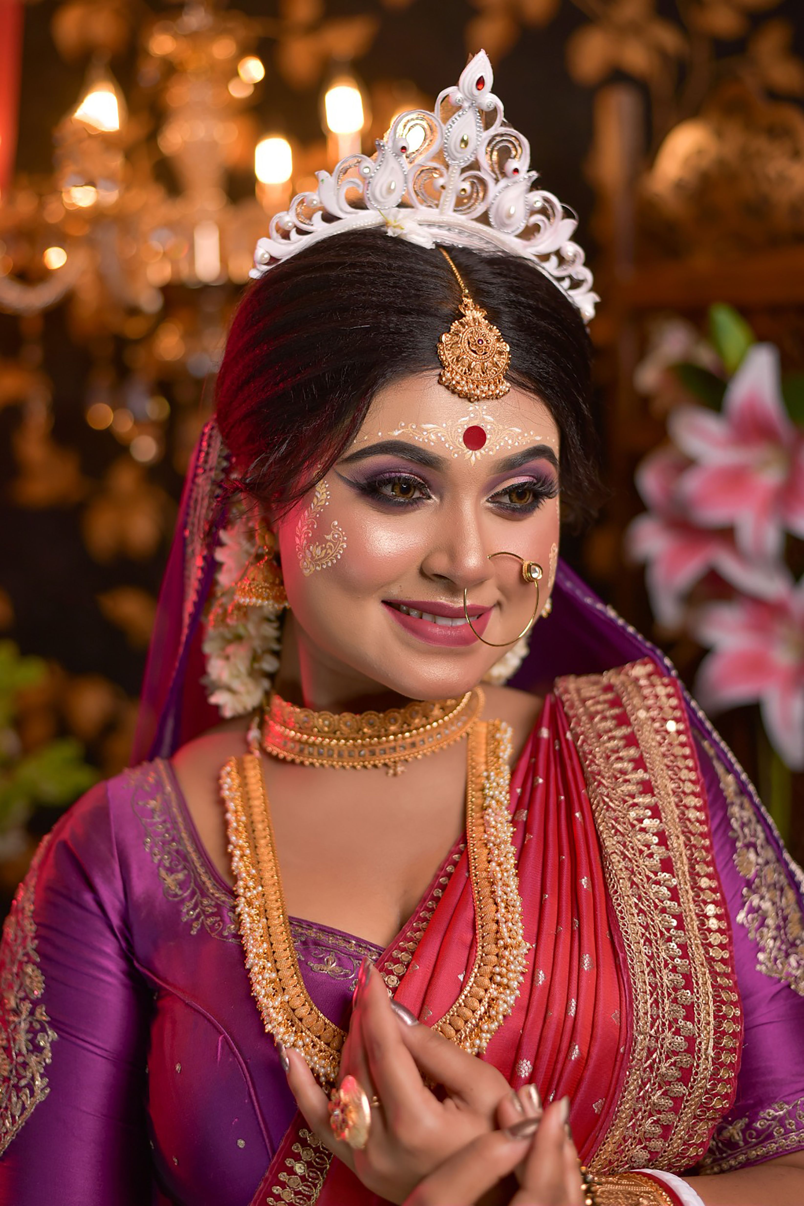 An elegant Bengali bride in a traditional saree, adorned with floral jewelry, smiling during a festive occasion.
