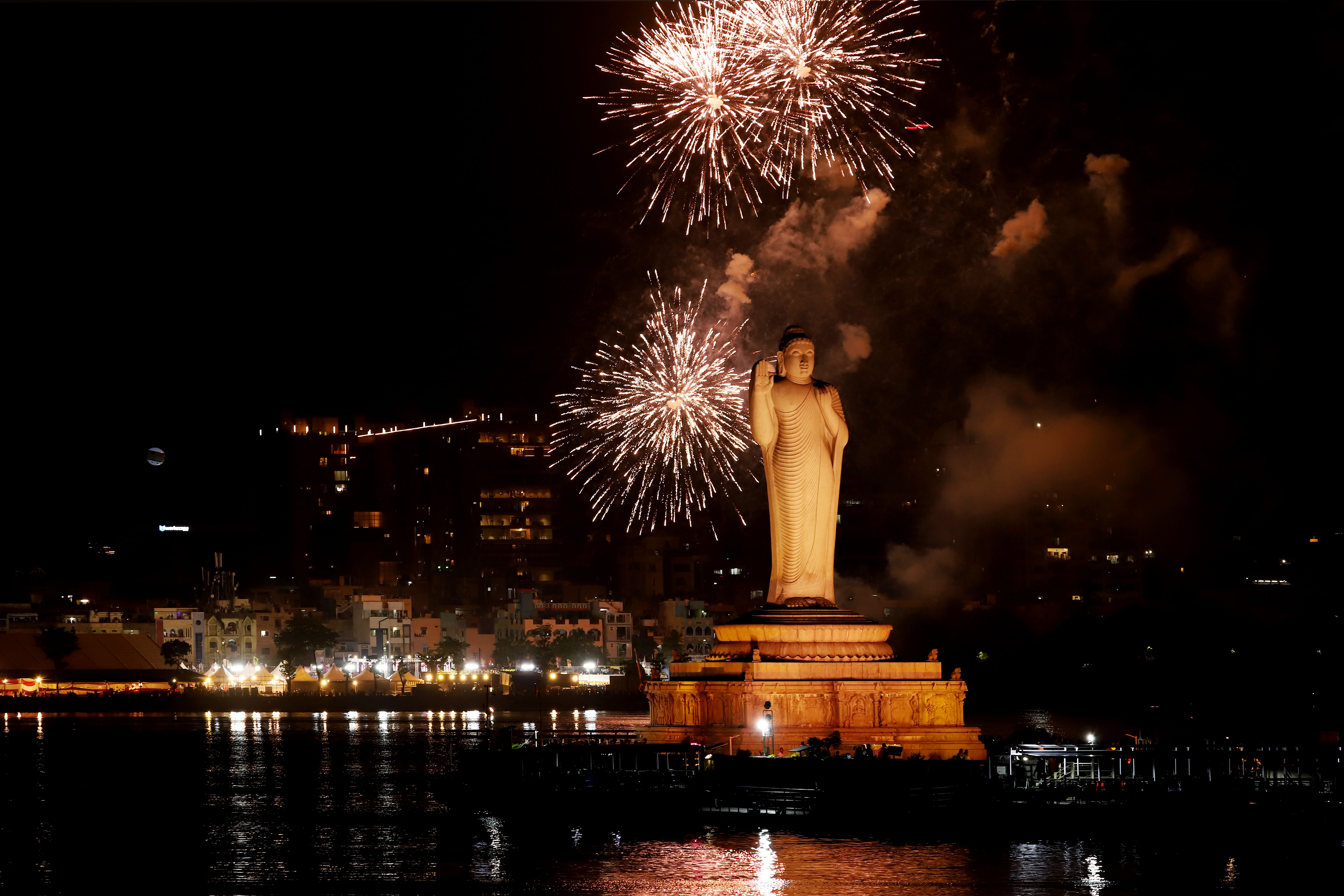 Breathtaking view of a Buddha statue illuminated by fireworks against a night sky.