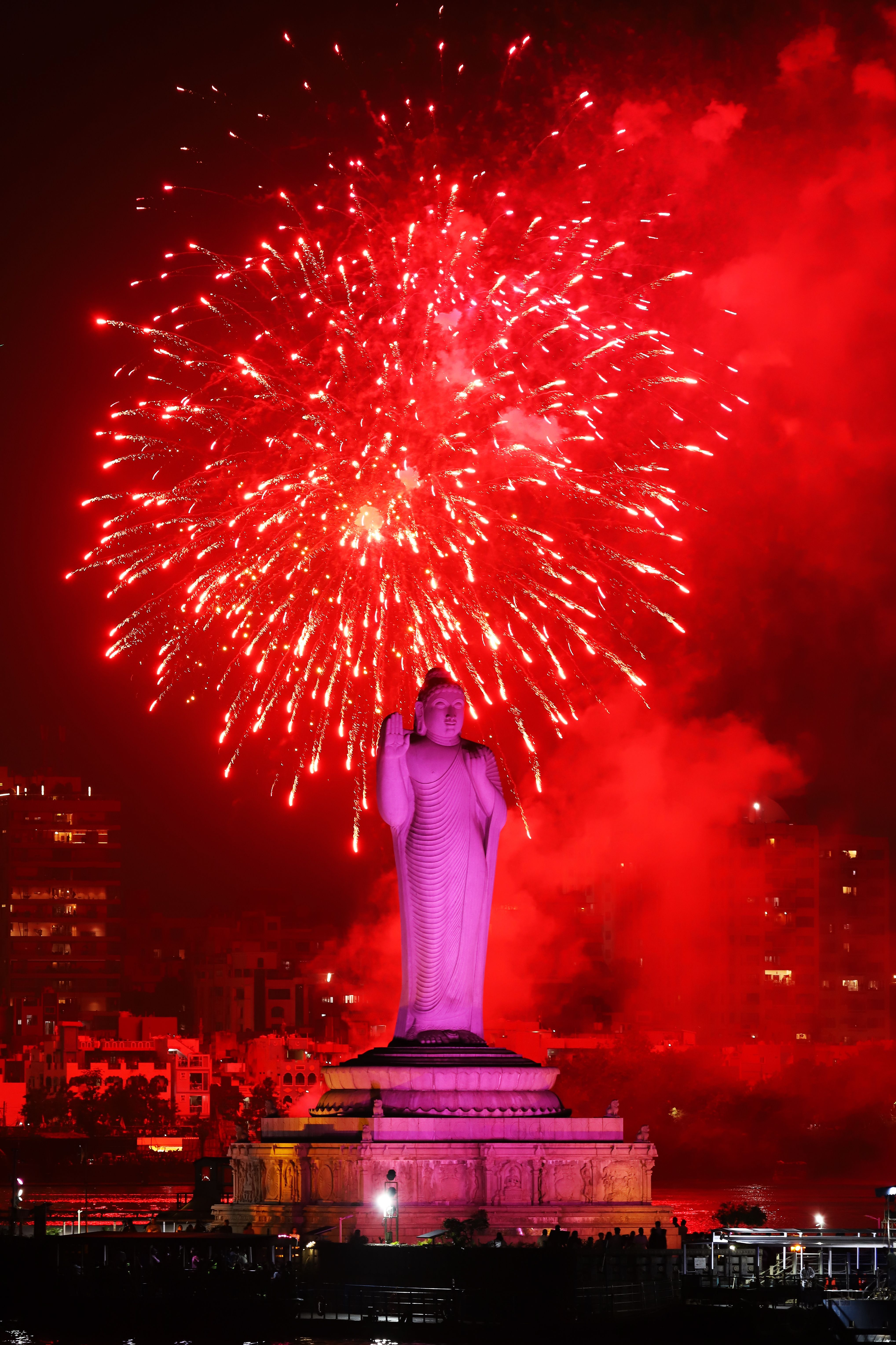 Stunning view of a Buddha statue illuminated by vibrant red fireworks against a night sky.