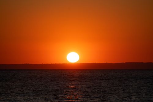 Free Beautiful sunset over the ocean with vibrant orange sky and calm waters. Stock Photo