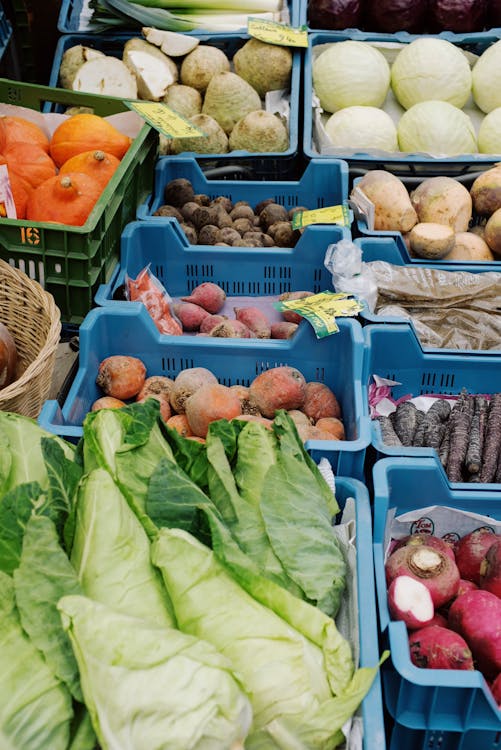 Plastic boxes with various fresh vegetables for sale on market stall