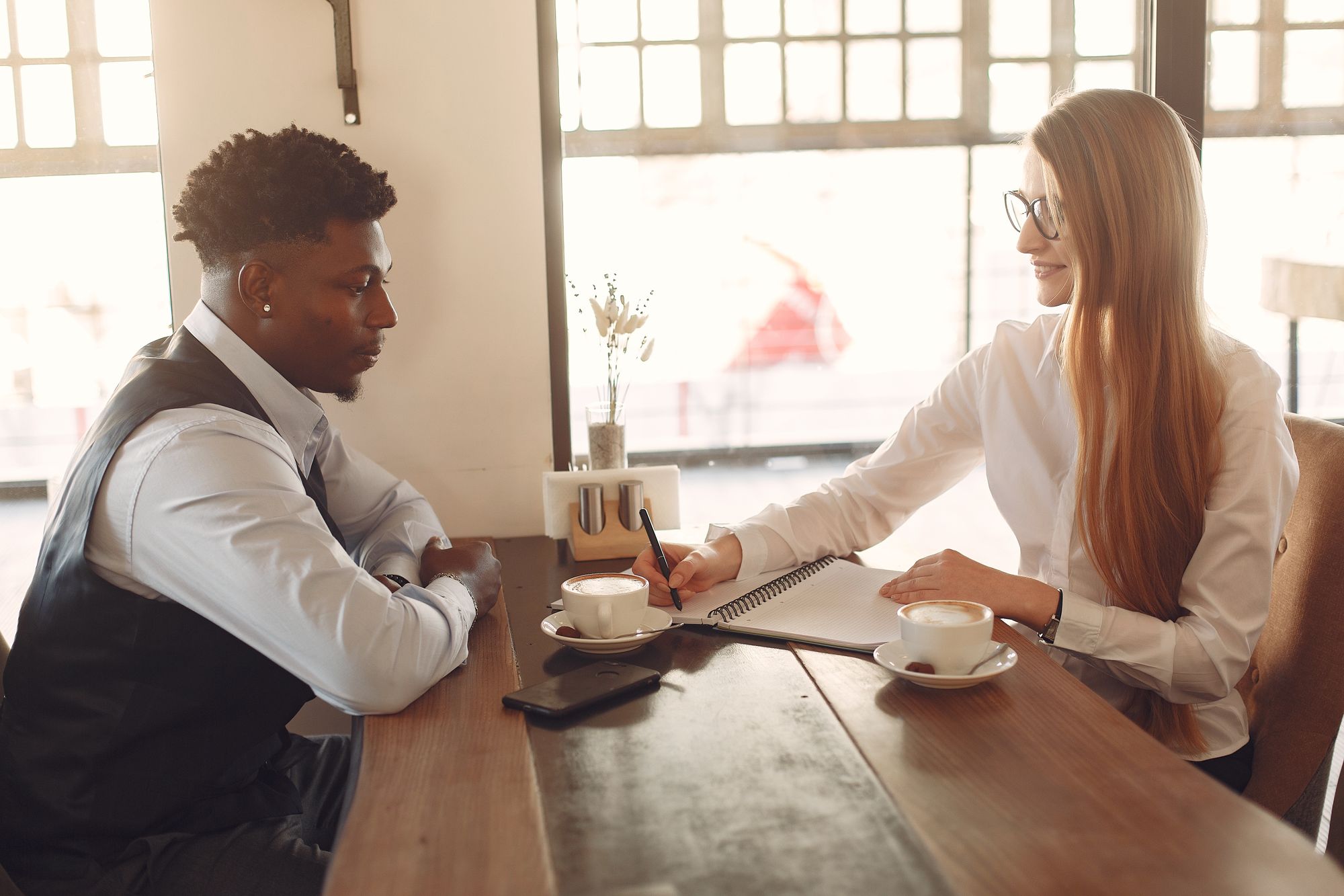 Two colleagues talking through ideas over coffee at a cozy cafe table.
