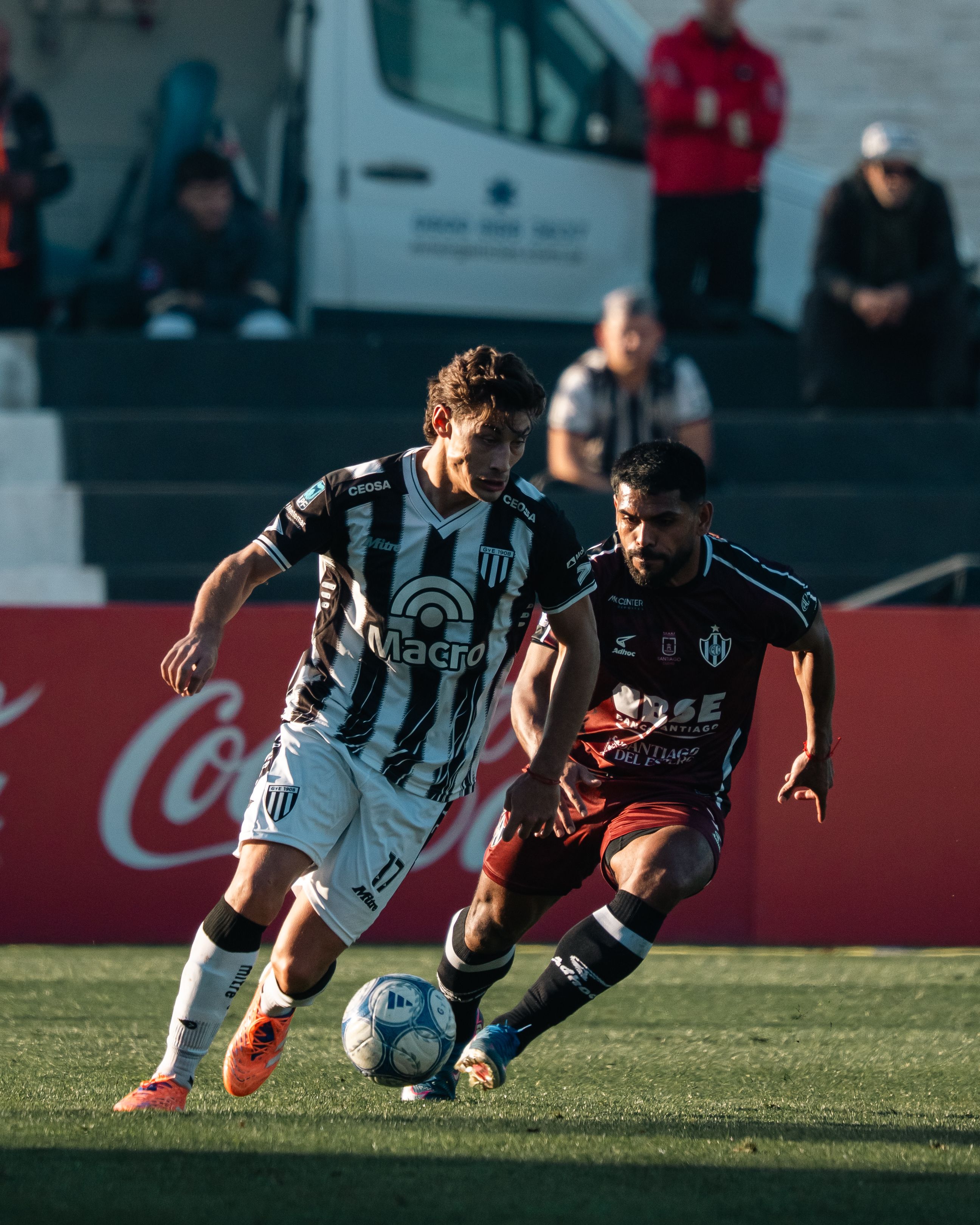 Twee voetballers strijden fel om de bal tijdens een wedstrijd in de middagzon.