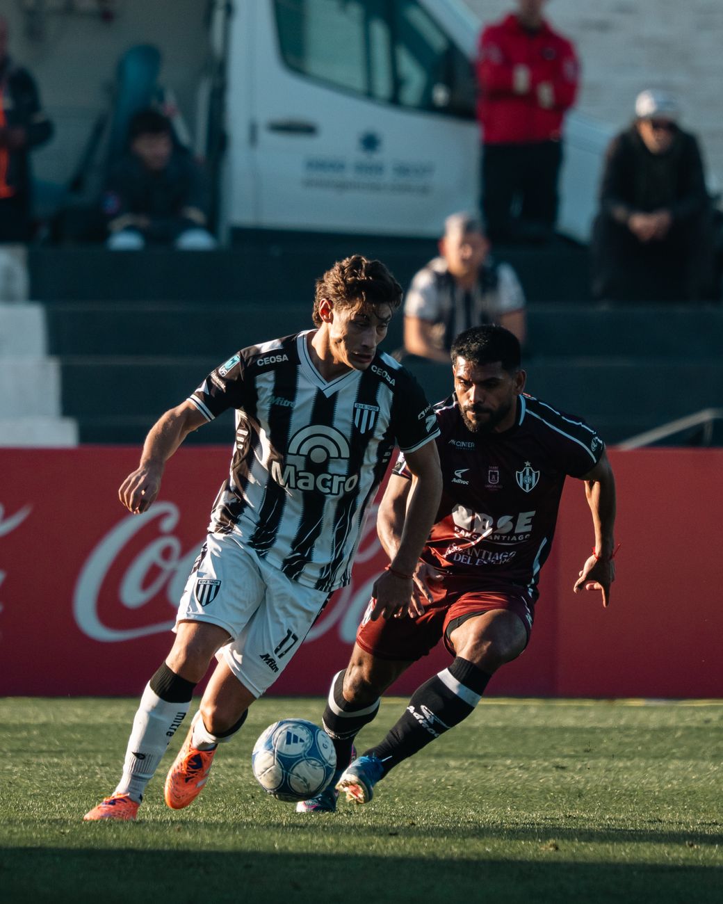 Twee voetballers strijden fel om de bal tijdens een wedstrijd in de middagzon.