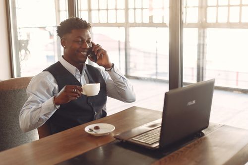Free A smiling businessman having a coffee while speaking on the phone in a modern office with a laptop. Stock Photo