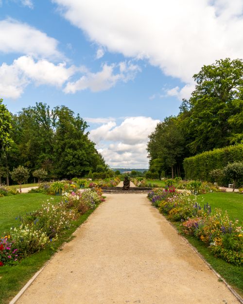 Free A scenic garden path with vibrant flowers and lush greenery under a bright blue sky. Stock Photo