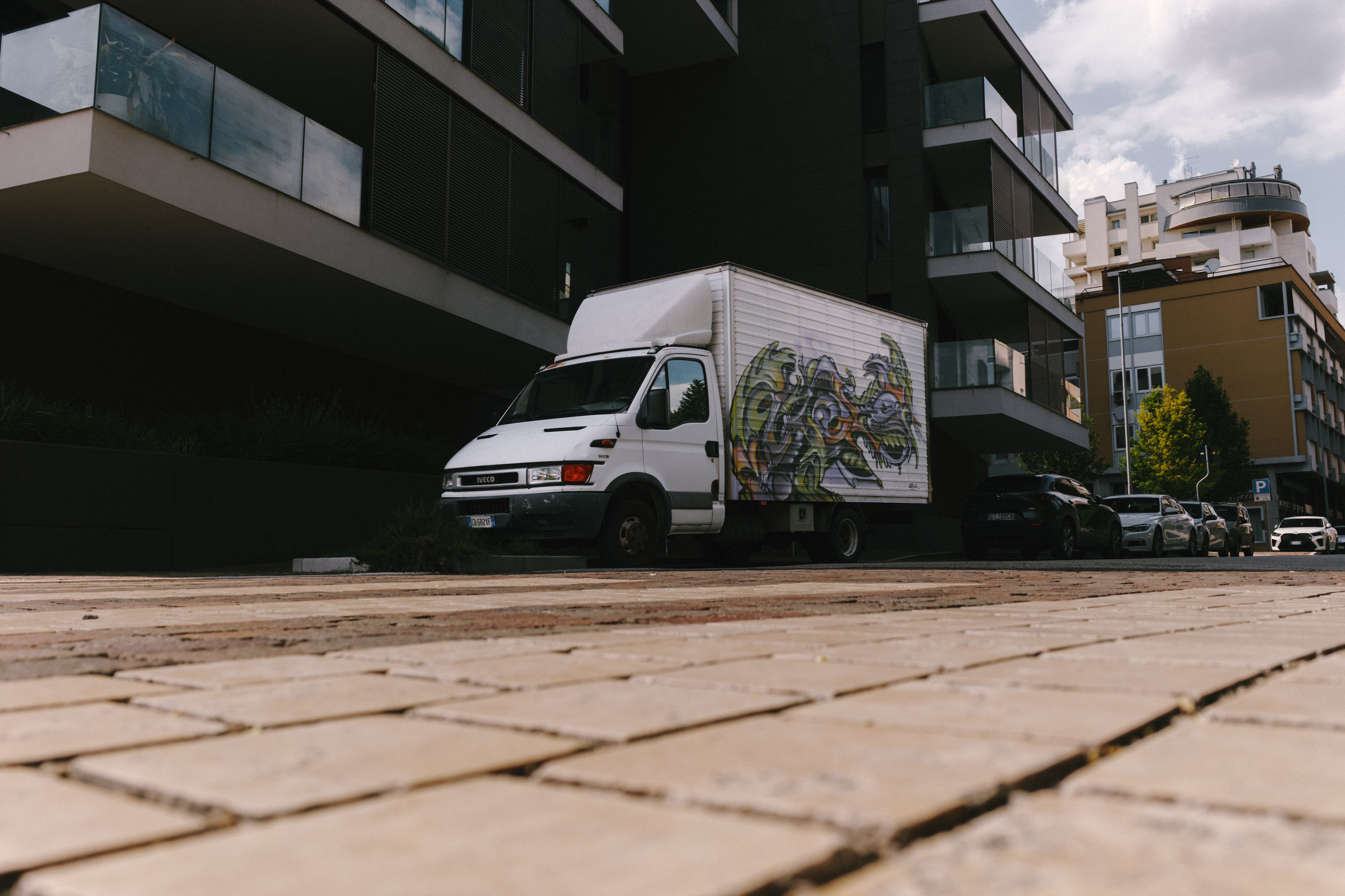 Street-level view of a graffiti-covered truck parked in an Italian urban area, featuring modern architecture.