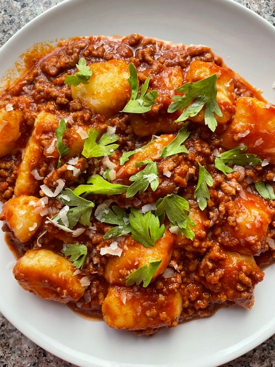Soft potato gnocchi in thick beef ragu topped with parsley leaves and shaved parmesan