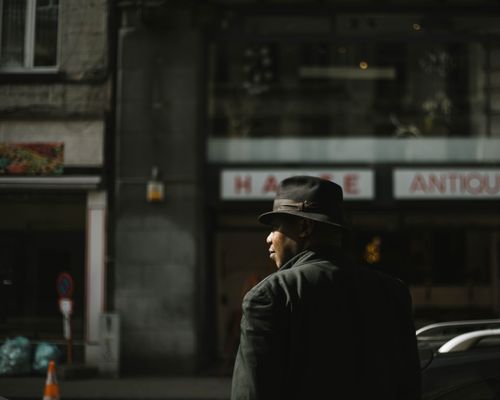 Free Man in black jacket and fedora walking in Brussels street. Urban scene with vintage vibe. Stock Photo