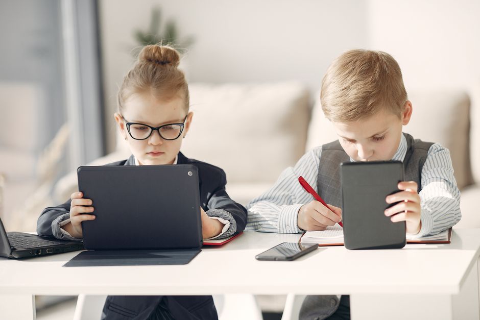 Niños vestidos como profesionales de negocios usando tablets y smartphones en interiores.