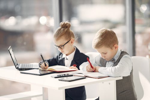 Serious preschool managers in uniform planning schedule in notebooks while sitting in front of modern devices in contemporary workplace