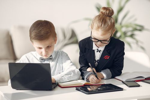 Free Serious business kids in formal wear taking notes in planner while working on netbook together in contemporary office behind sofa Stock Photo