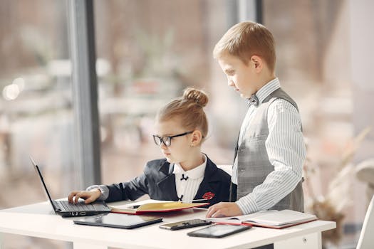 Two children dressed formally using a laptop in a bright office setting, mimicking business professionals.