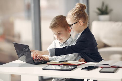 Adorable preschool coworkers using netbook and discussing project in light office