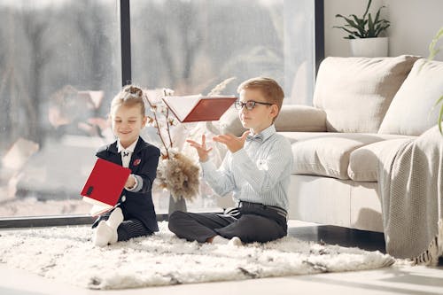 Happy little students throwing up textbooks in cozy living room