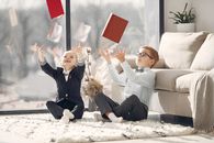 Cute children coworkers in uniform and eyeglasses throwing up organizers and laughing after working day in cozy atmosphere at home