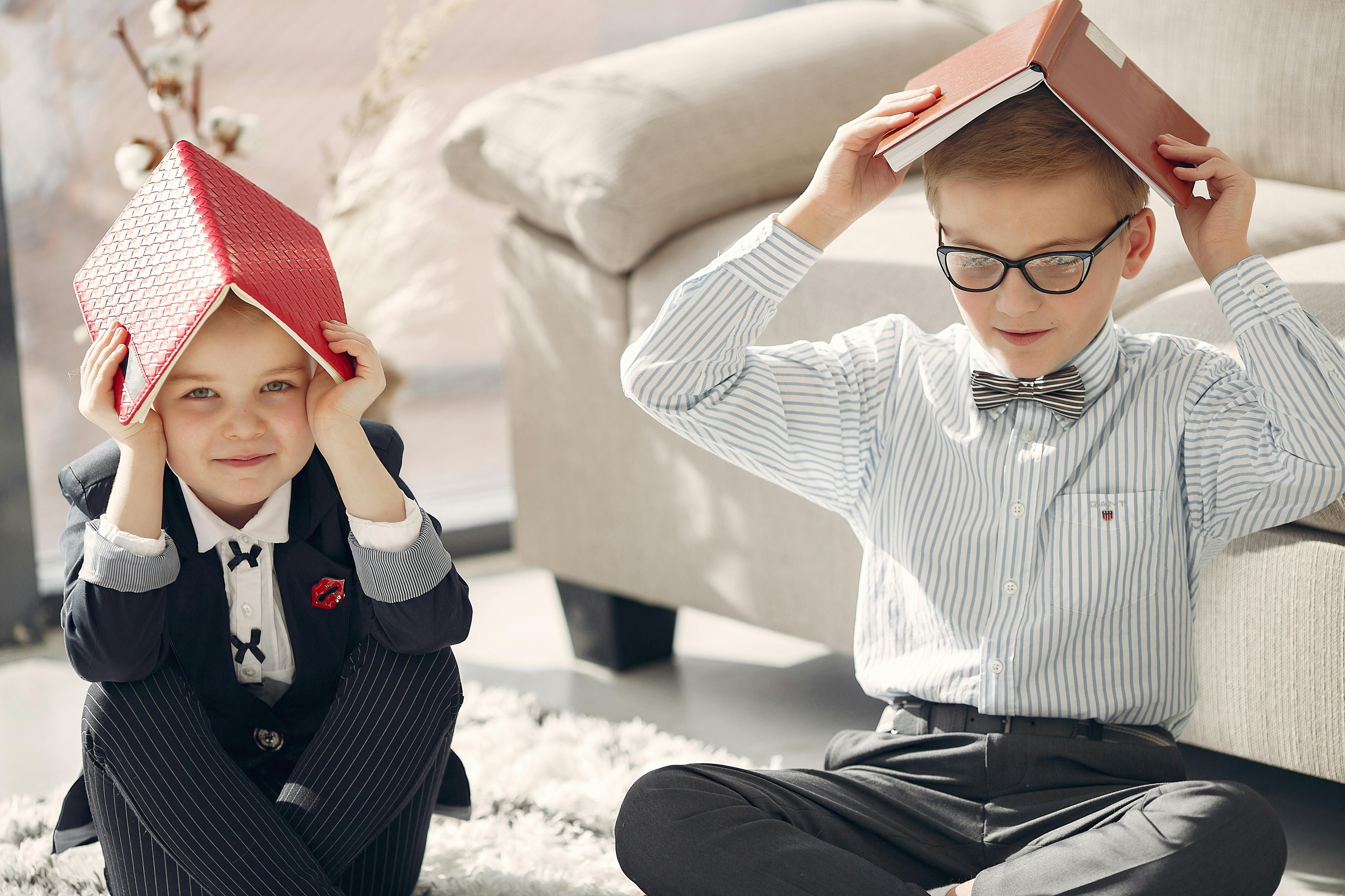 positive cute kids sitting with books on heads near sofa in cozy living room