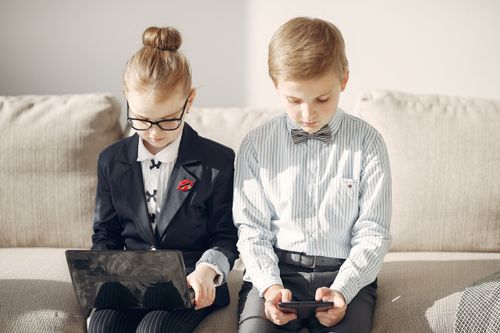 Free Focused preschool employees  in formal wear and eyeglasses using tablet and laptop while working online on project sitting on sofa at home Stock Photo
