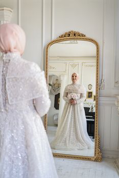 A bride in a luxurious wedding gown admires her reflection in an ornate mirror.