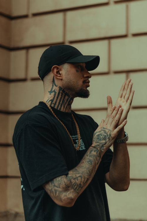 Free Profile of a tattooed man clapping with a confident pose in an urban setting. Stock Photo