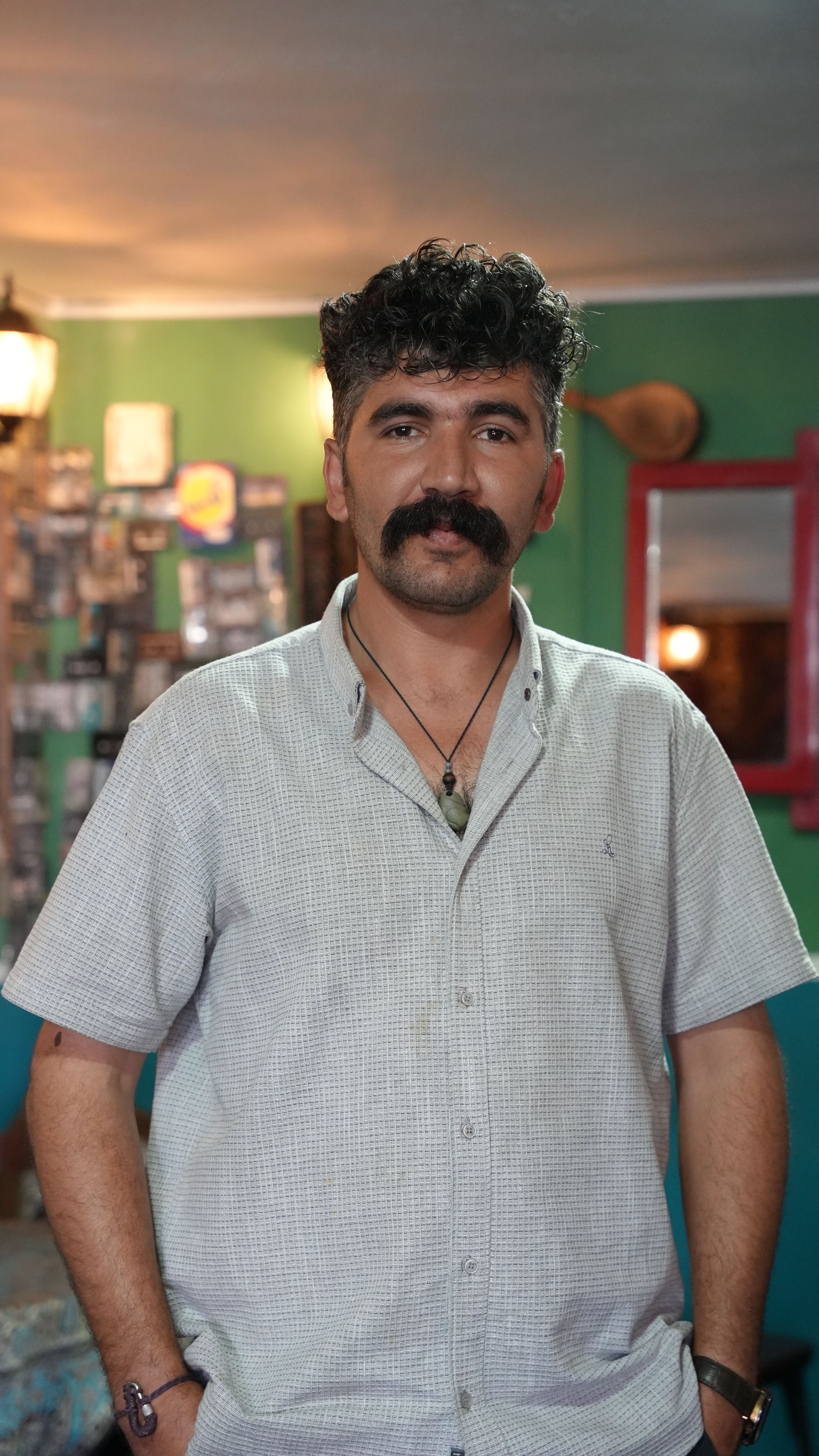 A middle-aged man stands confidently in a cozy cafe in Naqadeh, Iran, captured with warm ambiance.